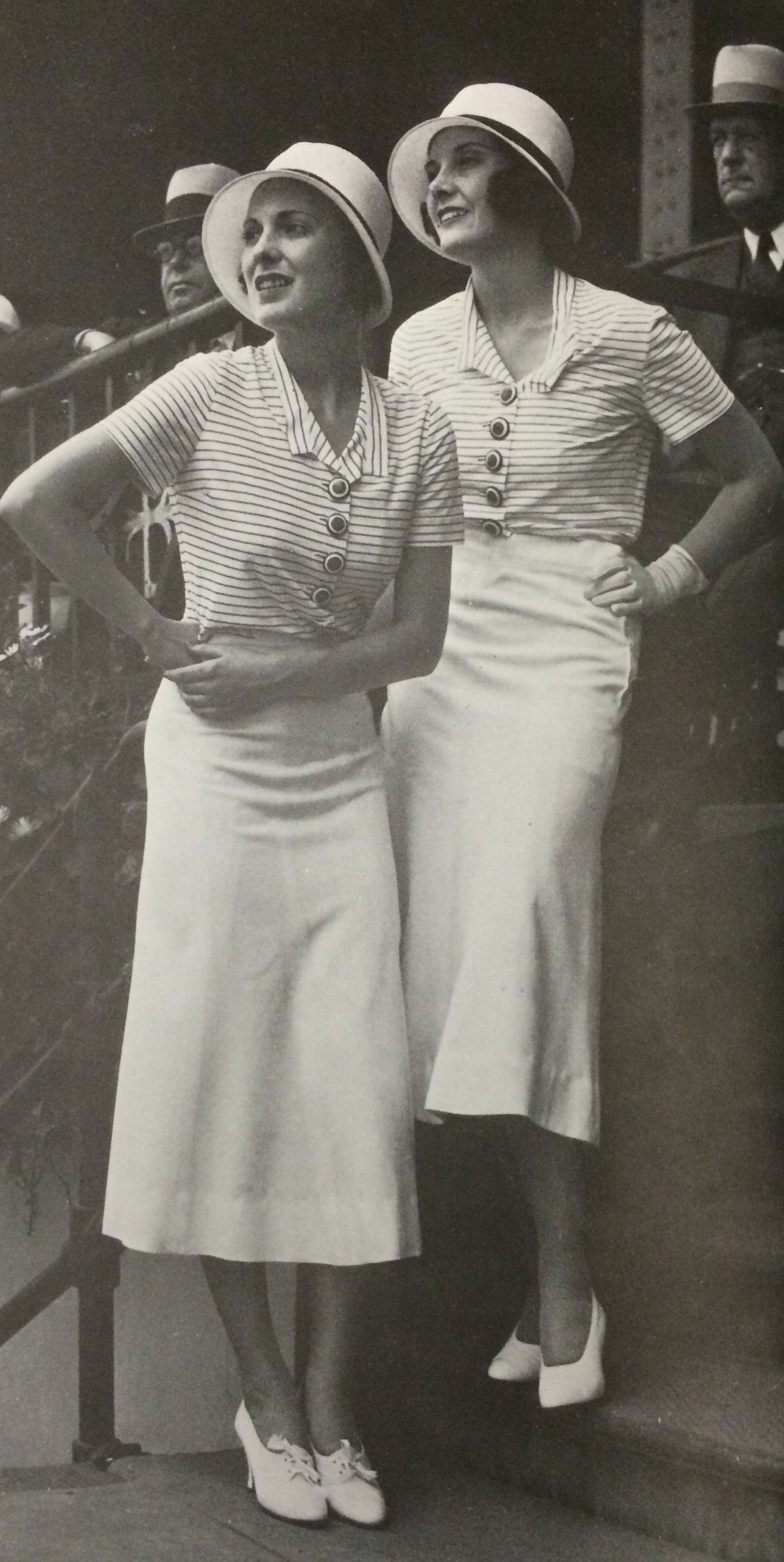 Two women wearing striped blouses, midi skirts, and cloche hats posing together outdoors.