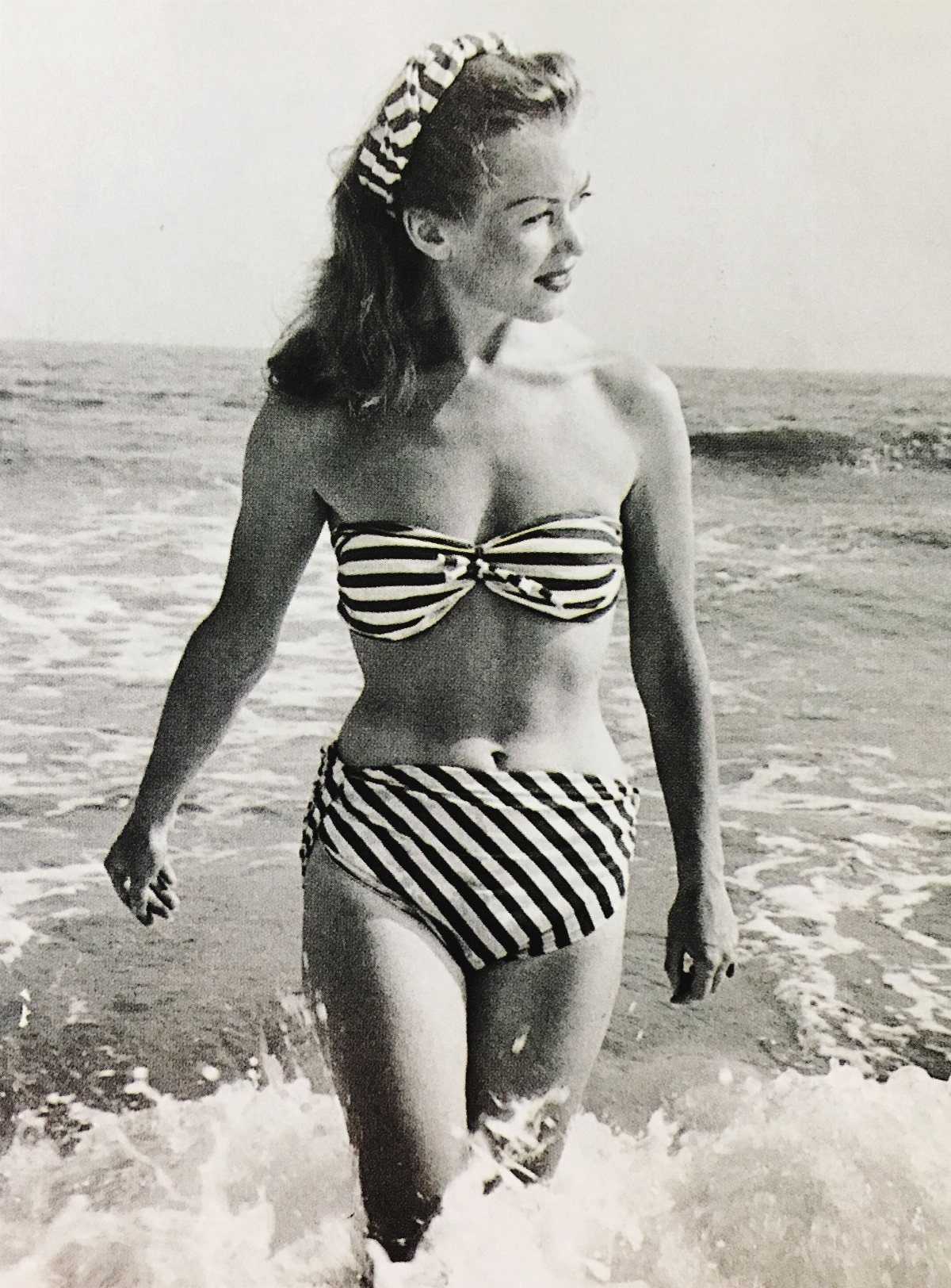 A woman in a striped two-piece bikini walking through ocean waves at the beach.