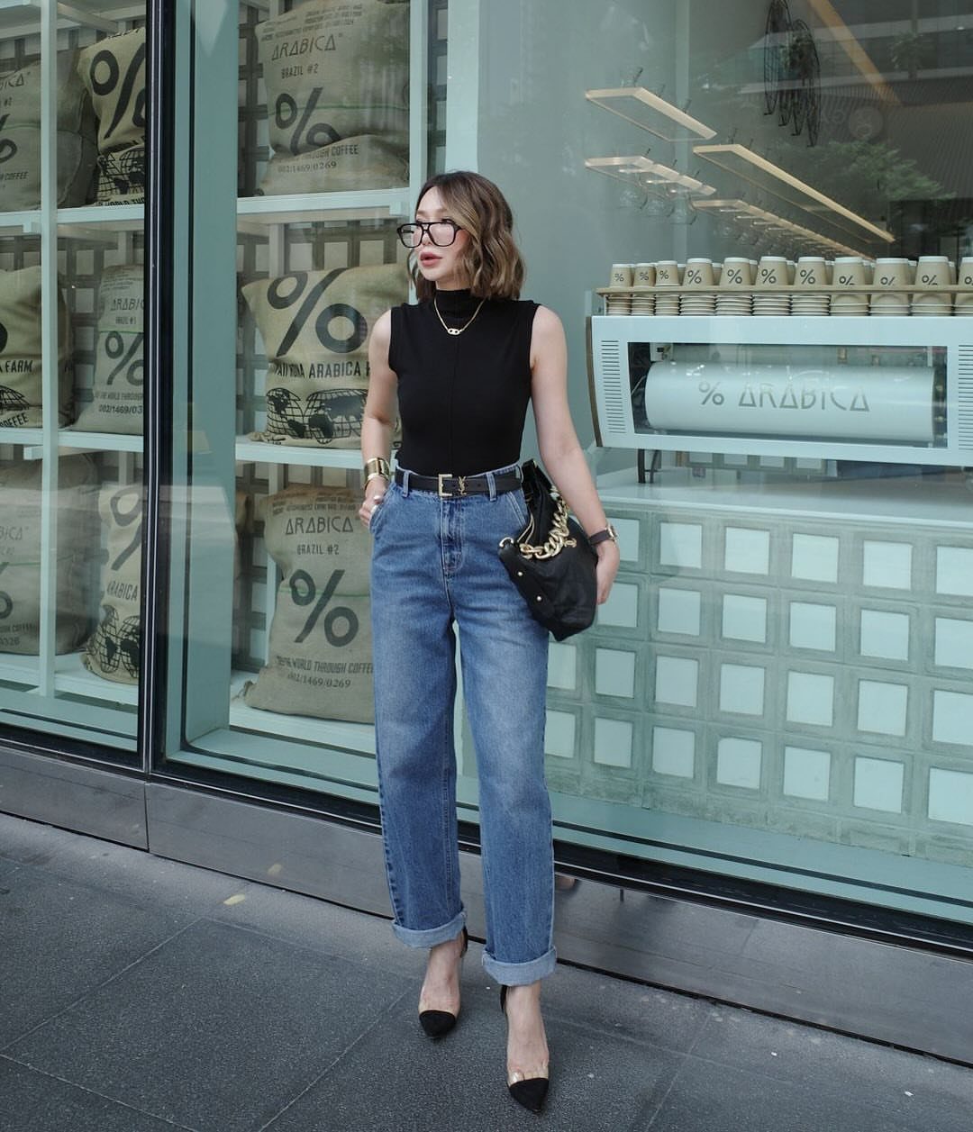 Woman wearing a black sleeveless top and blue boyfriend jeans with cuffed hems standing outside.