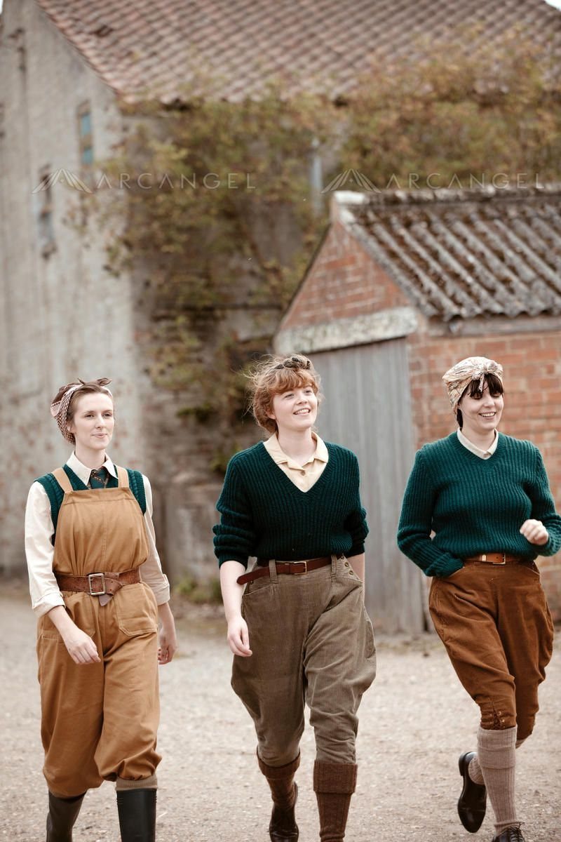 Three women walking in vintage utility clothing and high-waisted trousers outdoors.