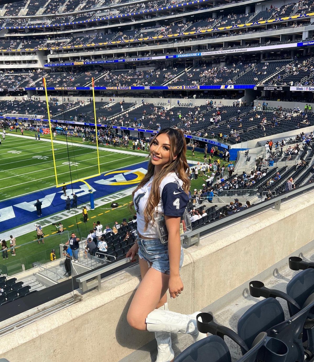 A woman in a sports jersey and denim shorts posing in a large football stadium.