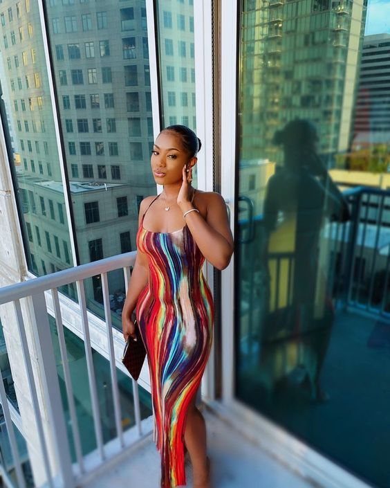 Woman in a vibrant rainbow print midi dress posing on a city balcony.