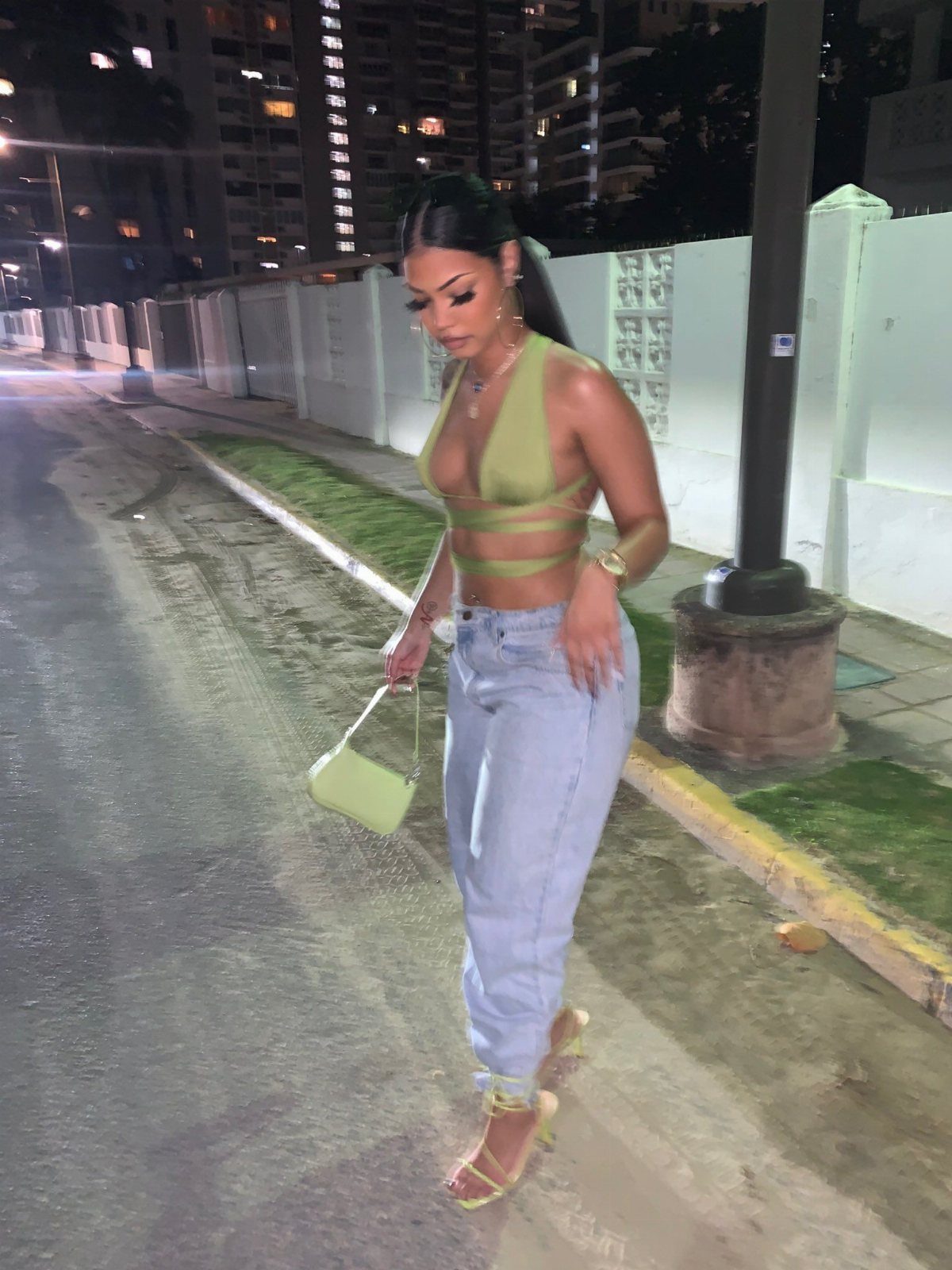 A woman wearing a sage green halter crop top and light blue jeans walking at night.