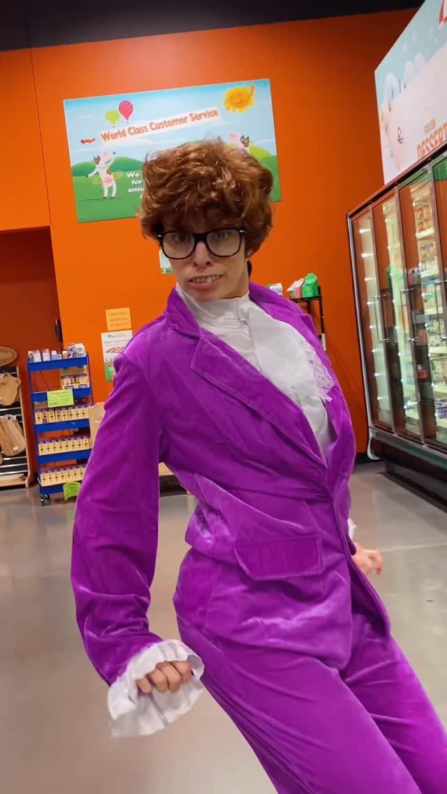 A person in a purple velvet suit and thick glasses posing in a store.