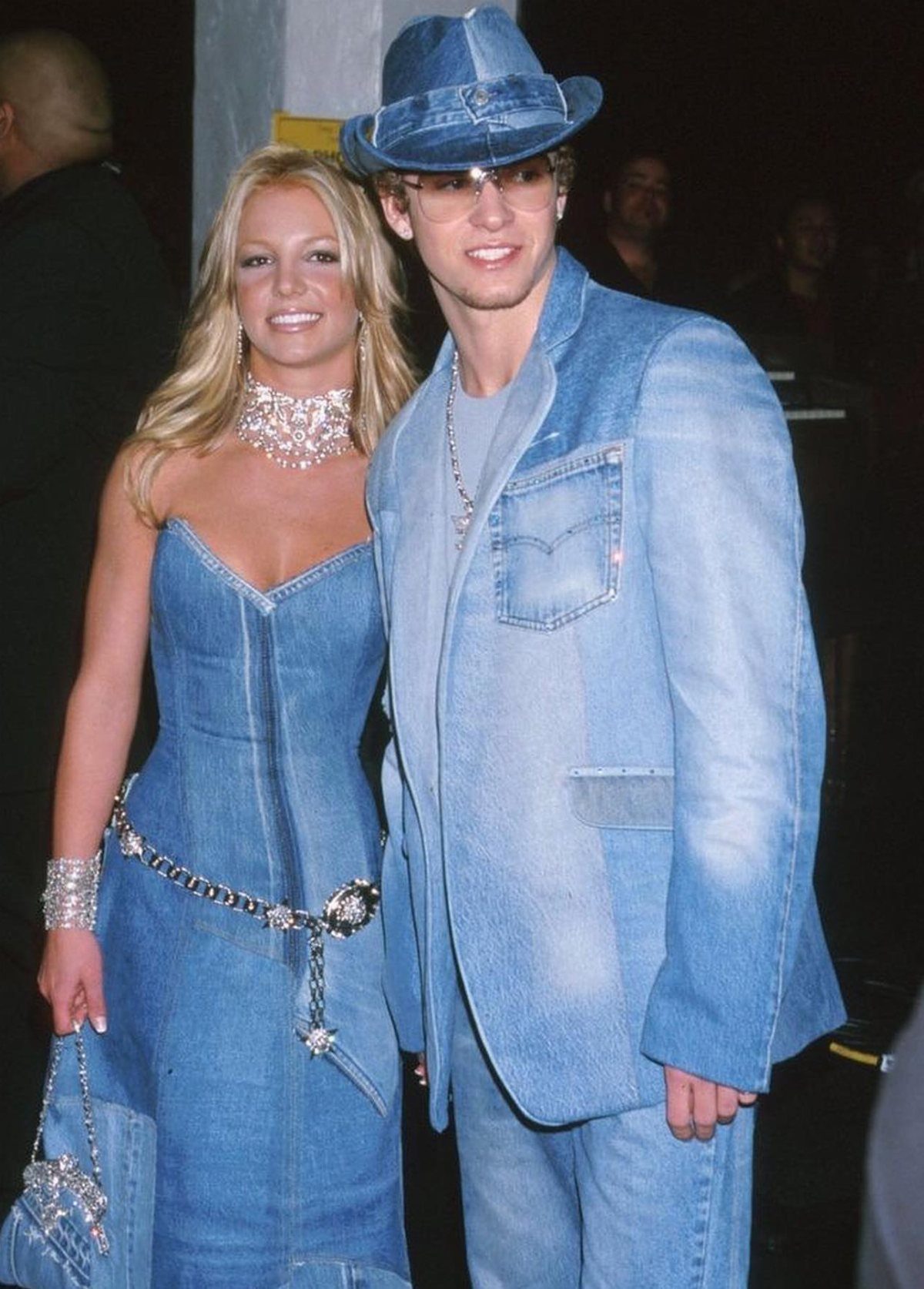 Blonde woman in a denim dress and man in a denim suit posing together.