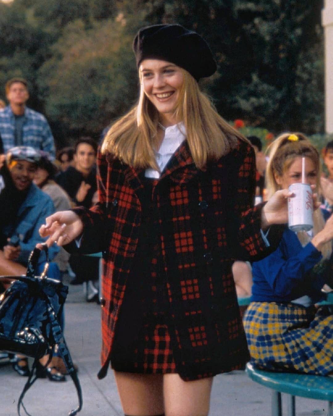 Blonde woman smiling in a red and black plaid suit and black beret outdoors.