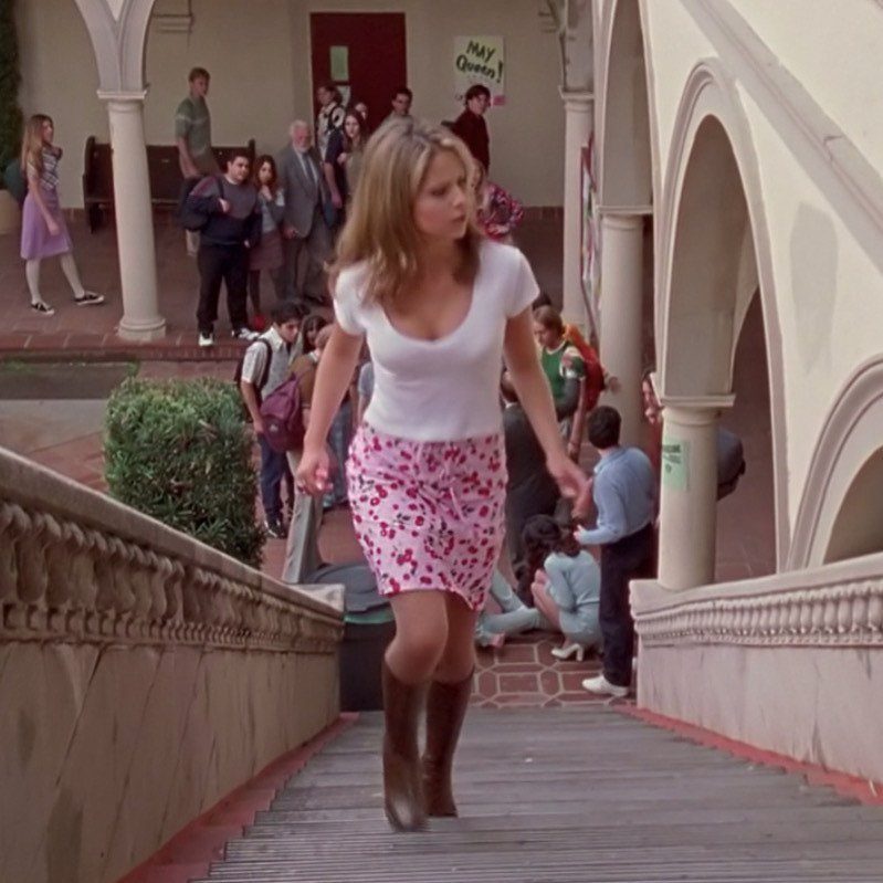 Woman in a white t-shirt and pink floral skirt walking down school stairs.