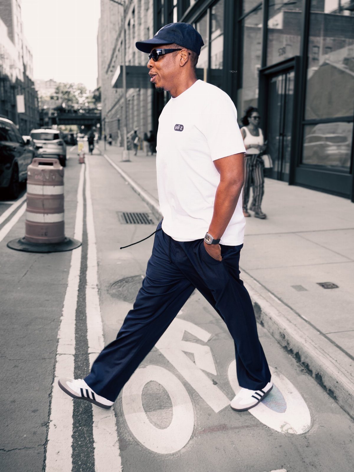 Man walking on a city street wearing a white t-shirt, navy trousers, and white Adidas Samba sneakers.