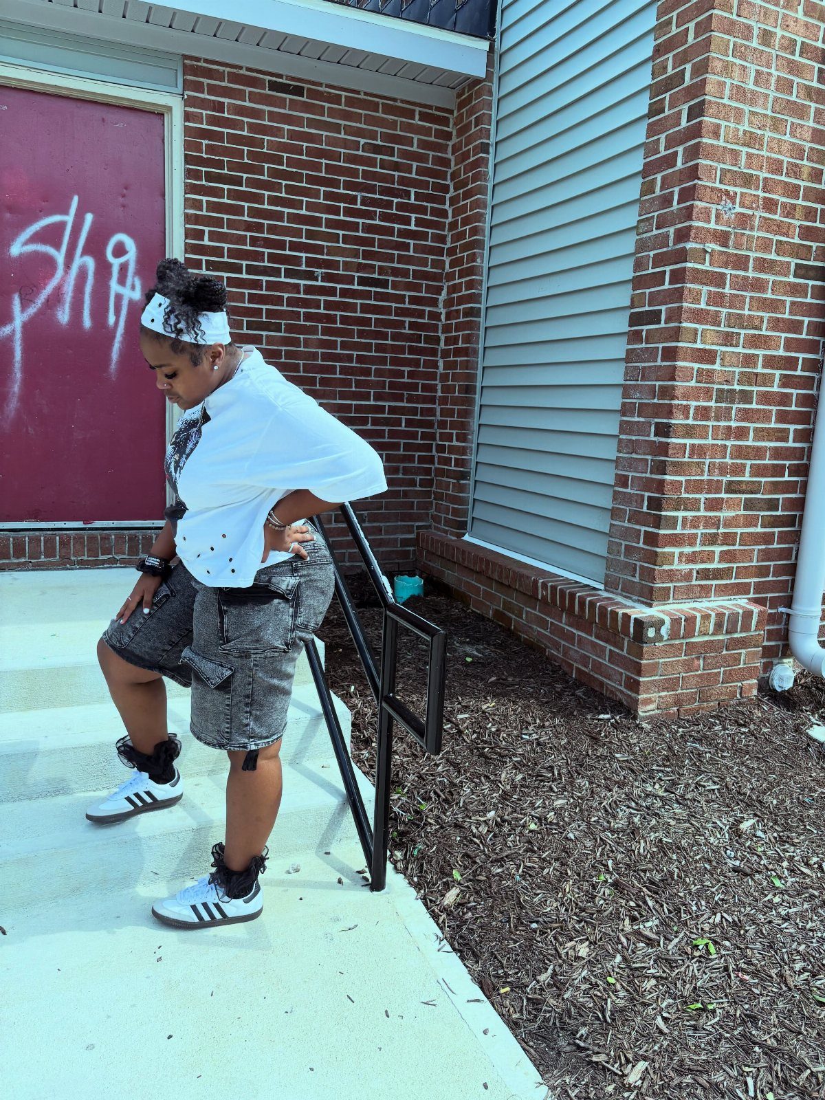 A person wearing an oversized white graphic tee, patterned shorts, and Adidas Samba sneakers.