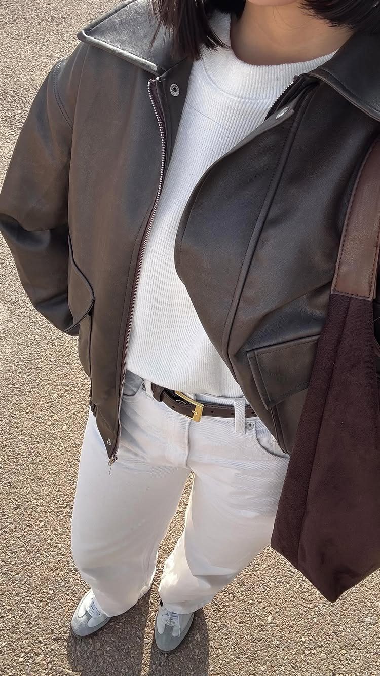 Person wearing a brown leather jacket, white sweater, white pants, and light blue Adidas Samba sneakers.