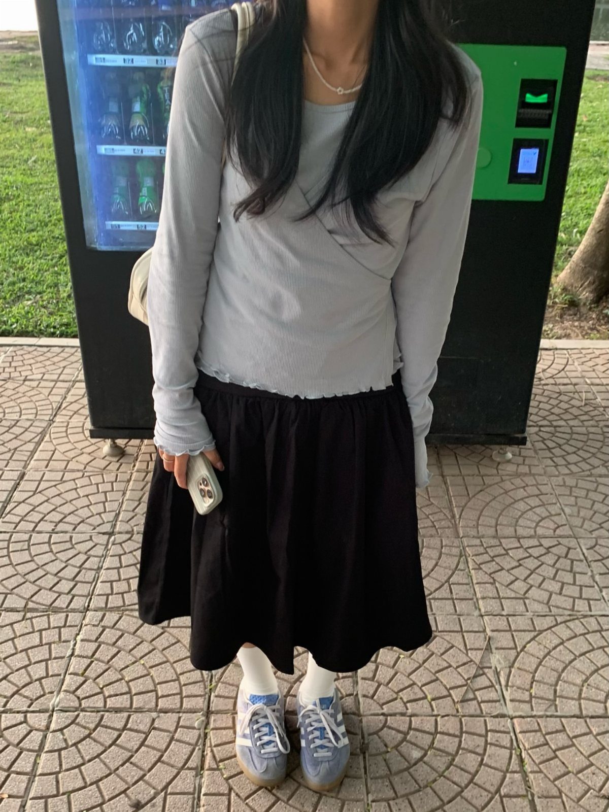 Person wearing a grey long-sleeved shirt, black midi skirt, and light blue Adidas Samba sneakers.