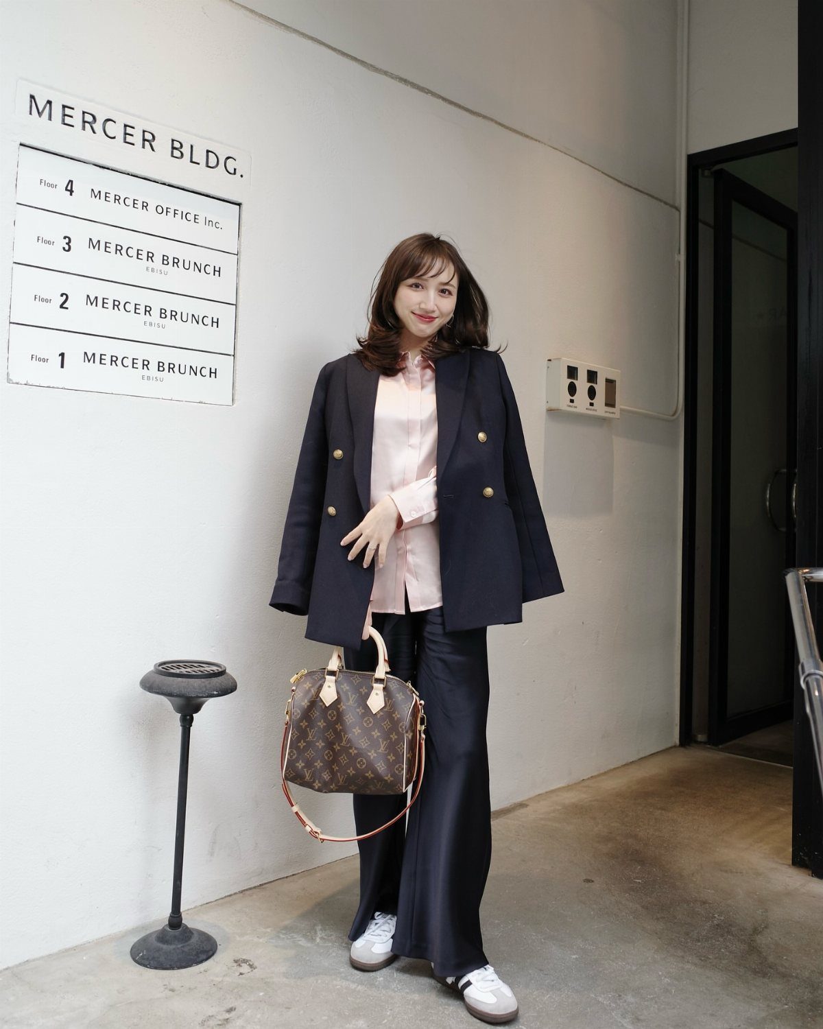 Woman wearing a navy blazer, pink shirt, and navy wide-leg trousers with white sneakers.