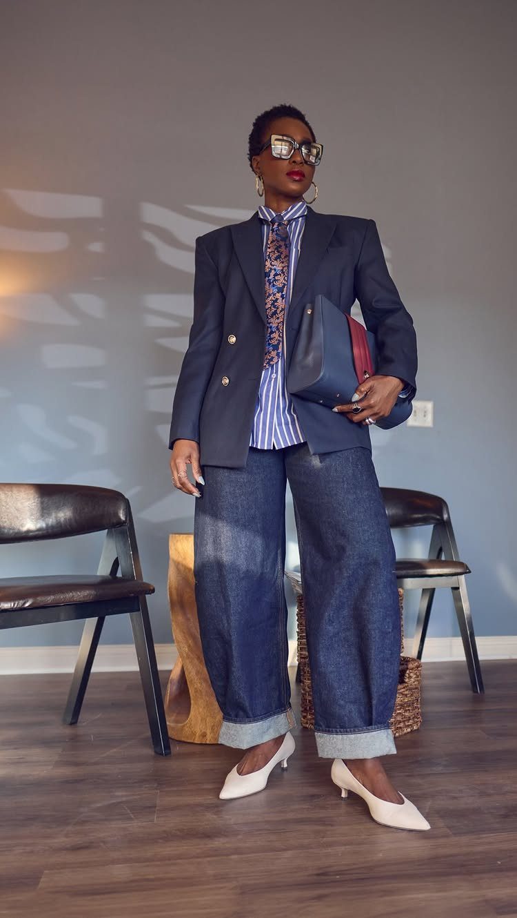 Woman posing in a navy blazer, striped shirt, wide-leg cuffed jeans, and white heels.