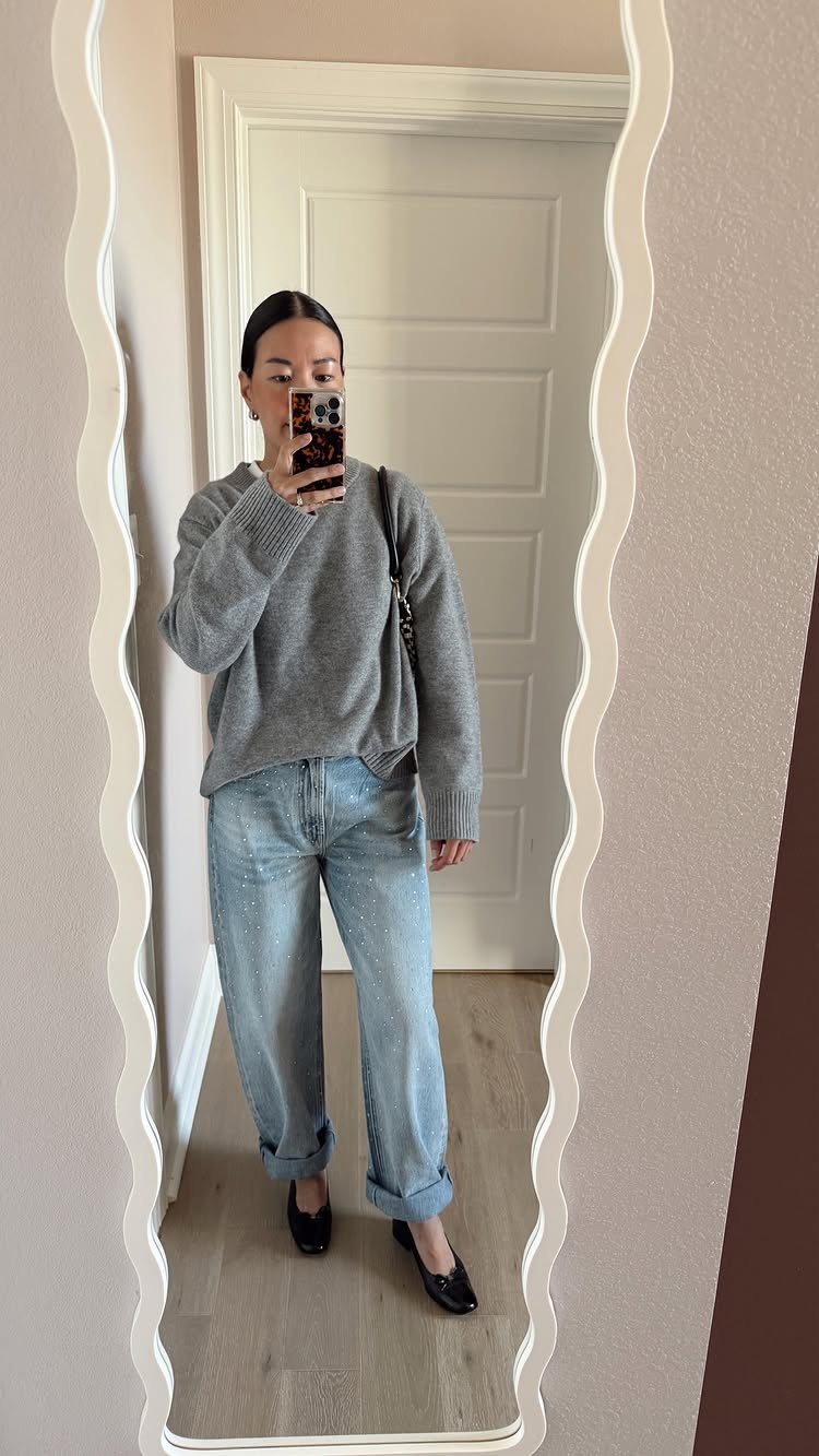 Woman in grey chunky knit sweater and light blue barrel jeans posing in a mirror.
