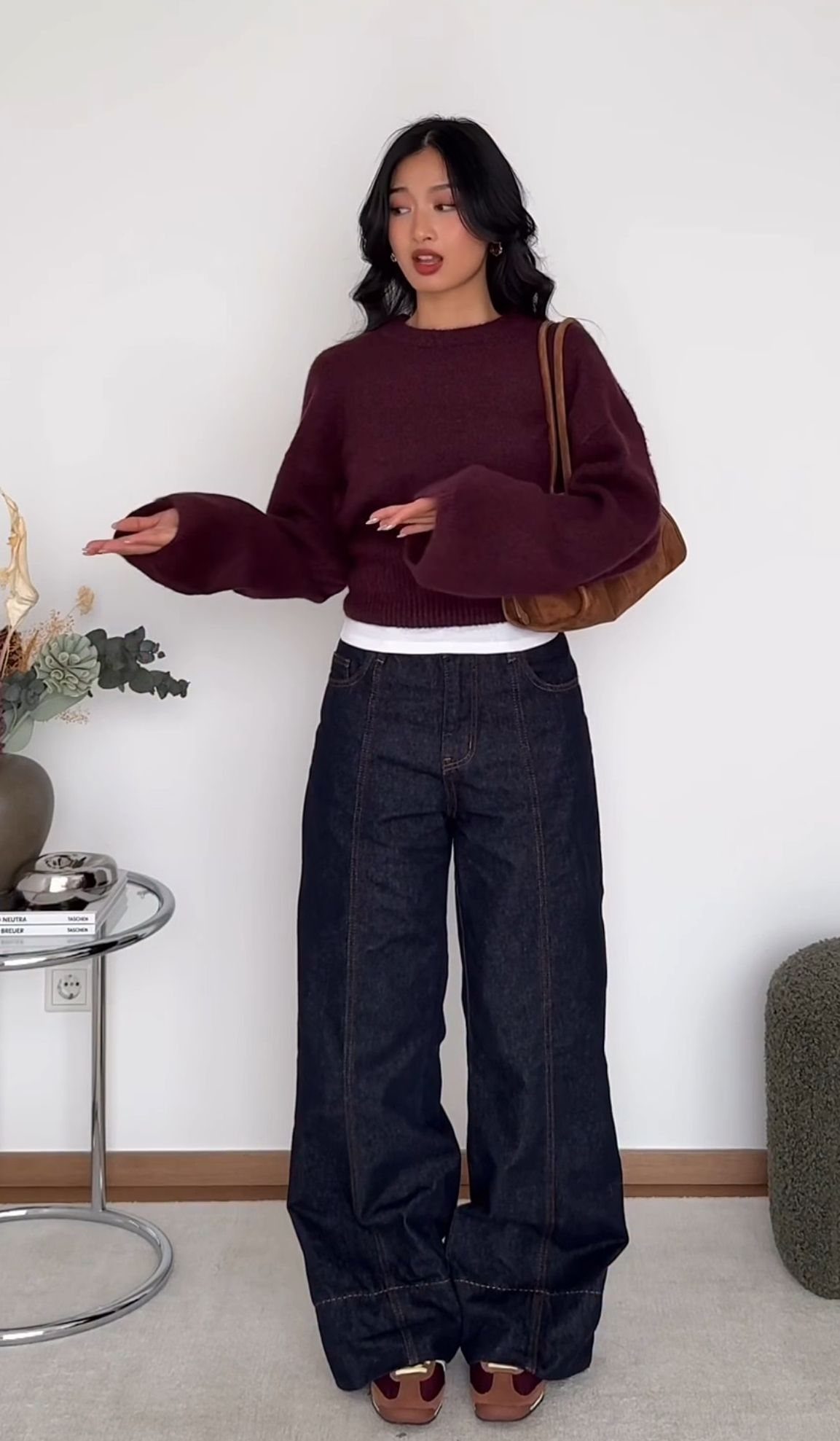 Woman posing in a burgundy cropped sweater and dark blue barrel jeans.
