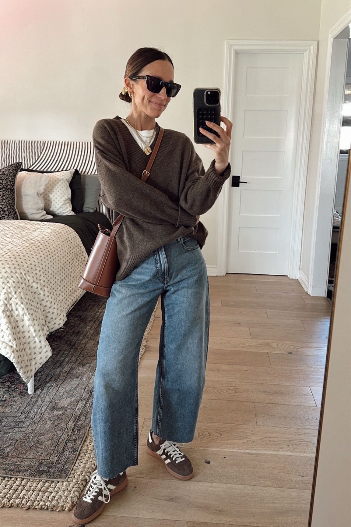 Woman in a brown sweater and blue barrel jeans wearing brown sneakers.