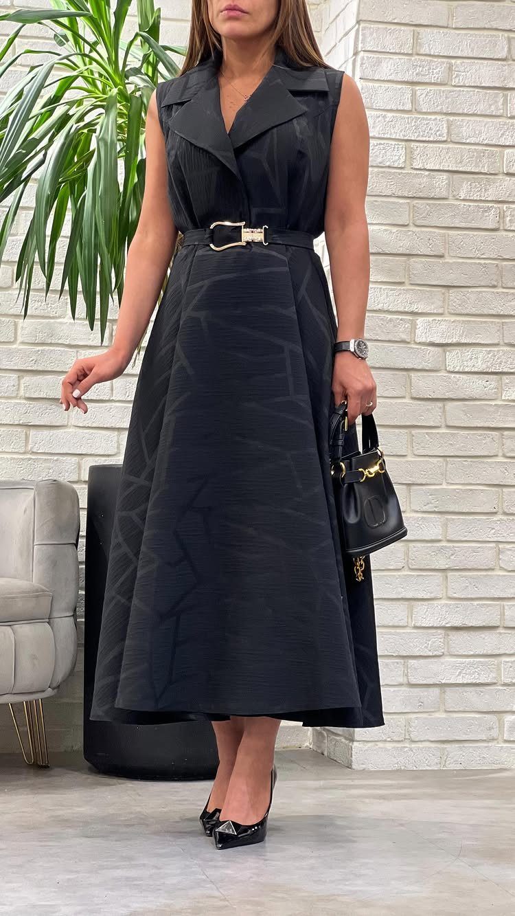Woman in a black sleeveless midi dress cinched with a gold-buckled belt.
