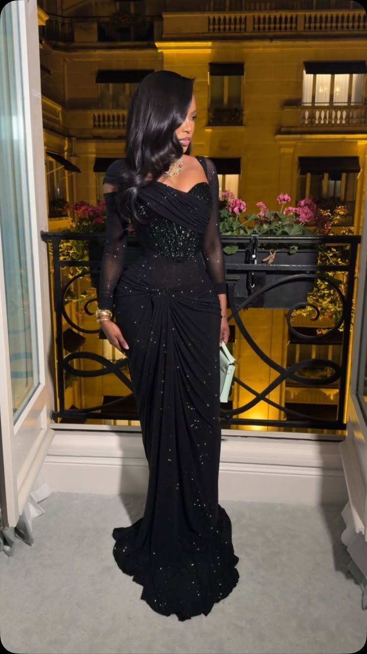 Woman in a long black shimmering evening gown posing on a balcony at night.