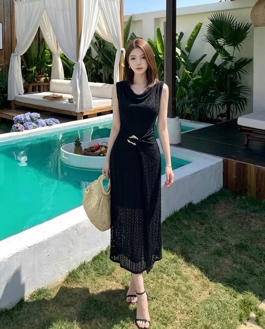 Woman in a black sleeveless midi dress standing by a swimming pool with a straw bag.