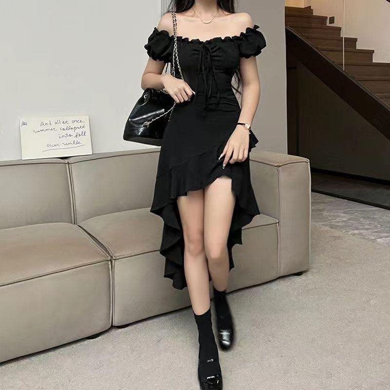 Woman in a black off-the-shoulder ruffled high-low dress standing near a beige sofa.