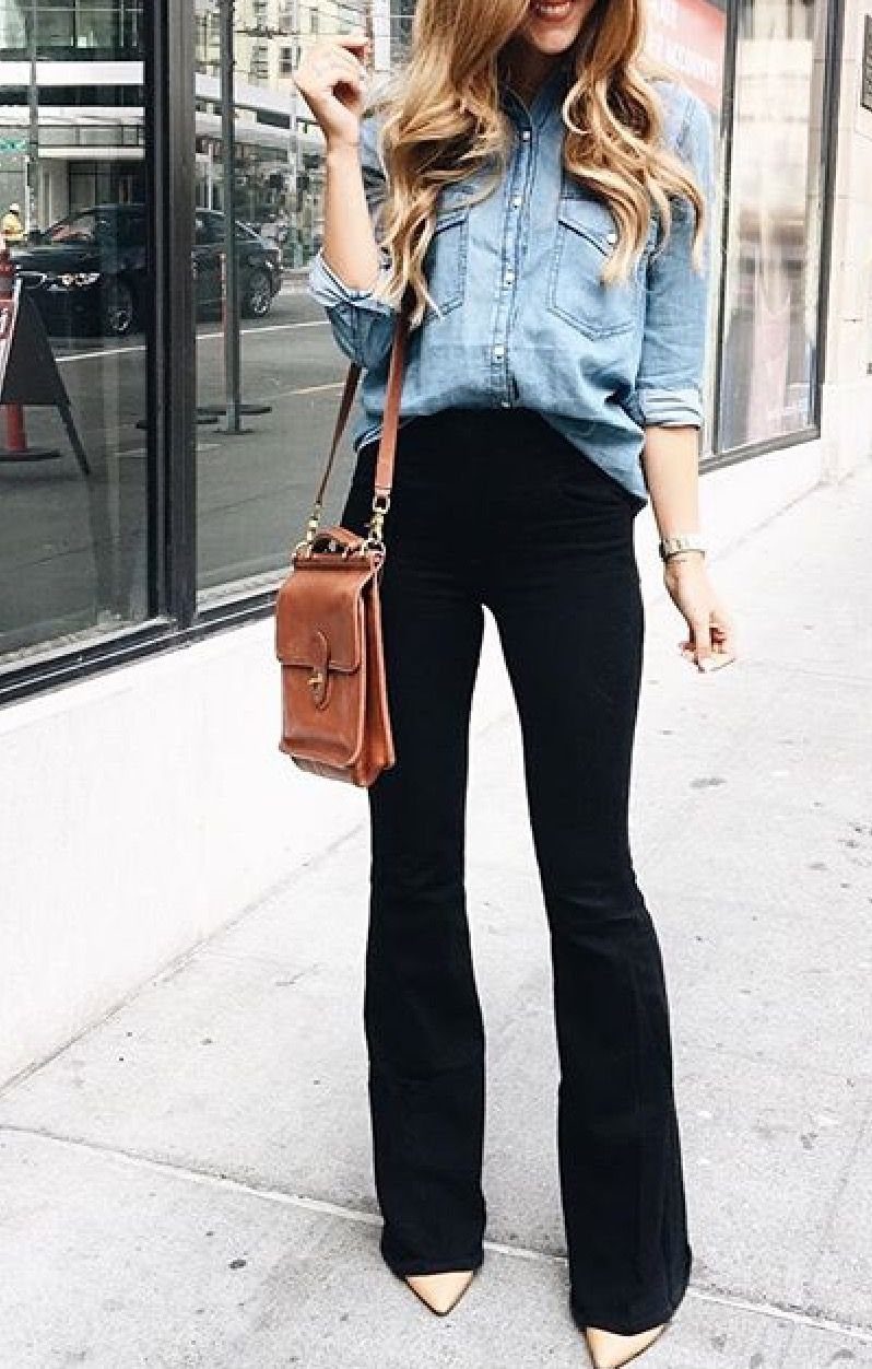 Woman wearing a light blue chambray shirt and black wide-leg pants standing on a sidewalk.