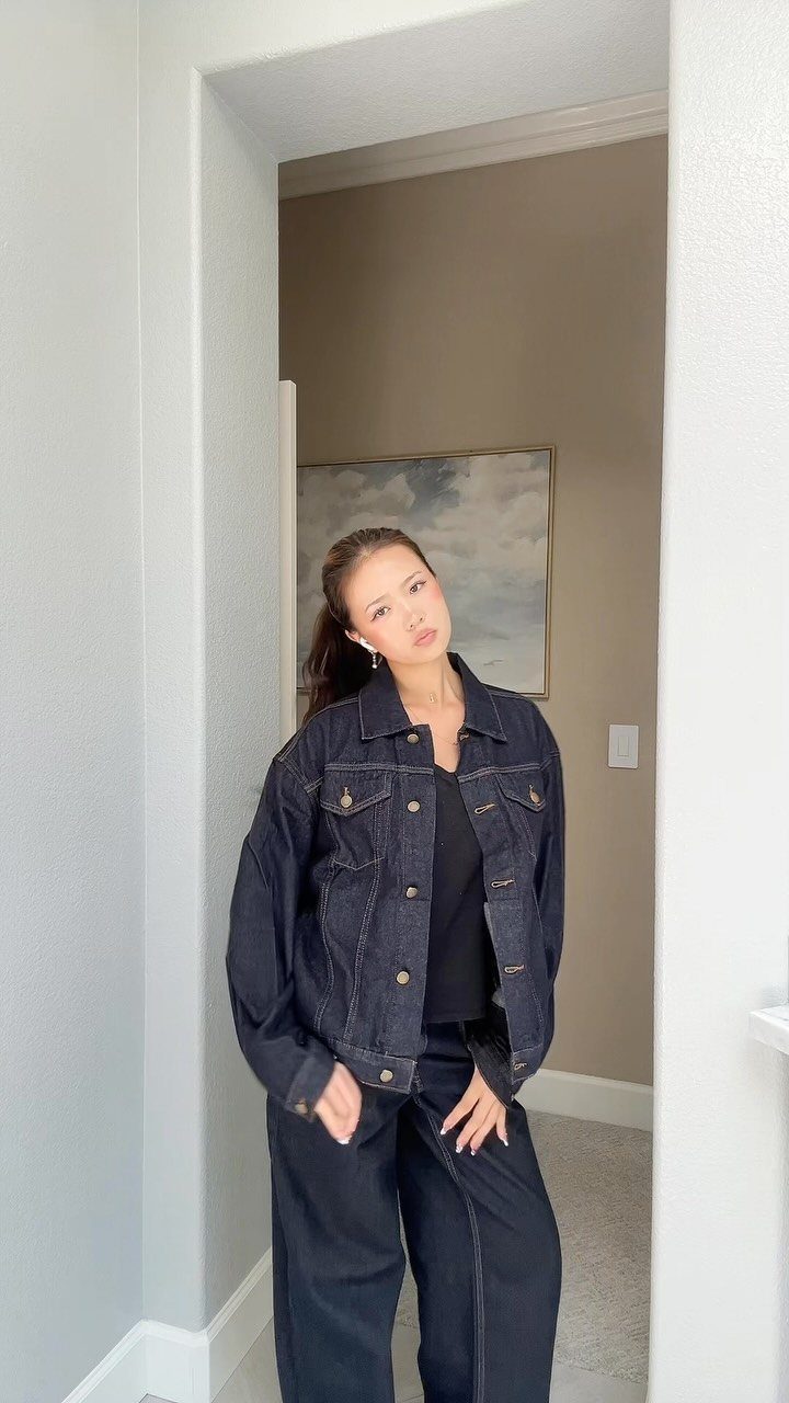 Woman wearing a dark denim jacket, black top, and black wide-leg pants standing in a doorway.
