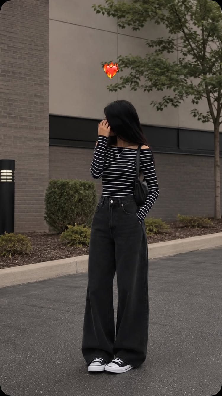 Woman wearing a black and white striped top with black wide leg jeans and sneakers.