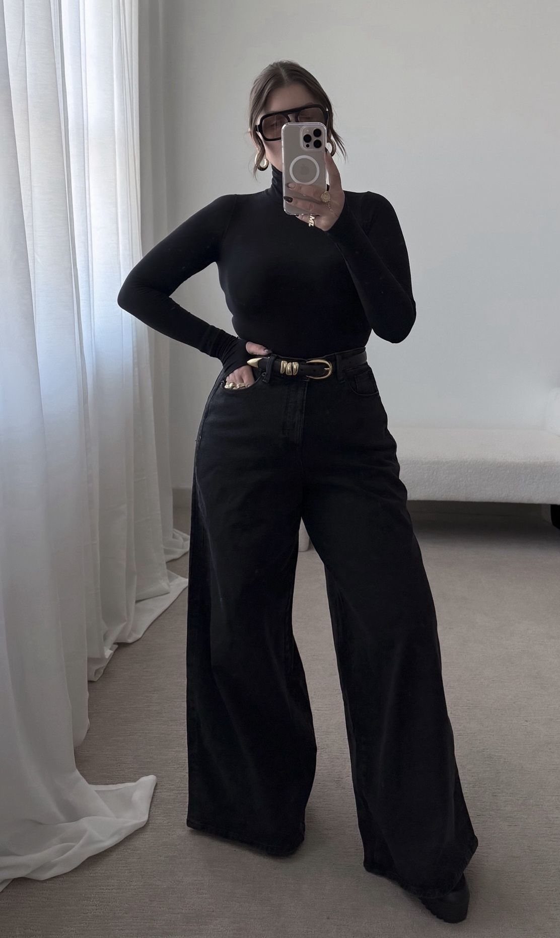 Woman in a black turtleneck and wide-leg jeans posing for a mirror selfie.