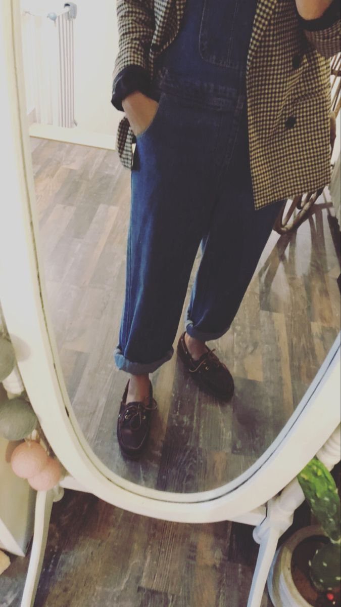 Person wearing denim overalls, a patterned blazer, and brown boat shoes standing on wood flooring.