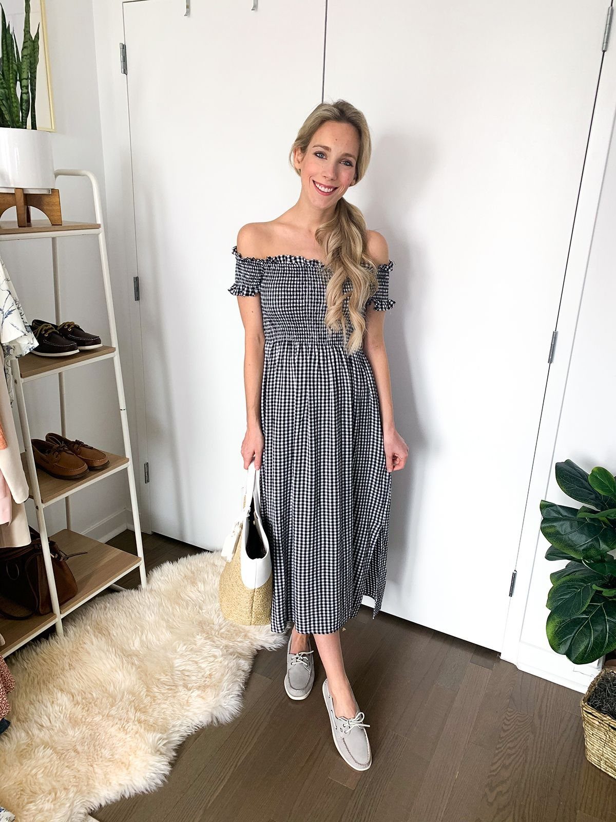 Woman in a black and white gingham off-the-shoulder midi dress and grey boat shoes.