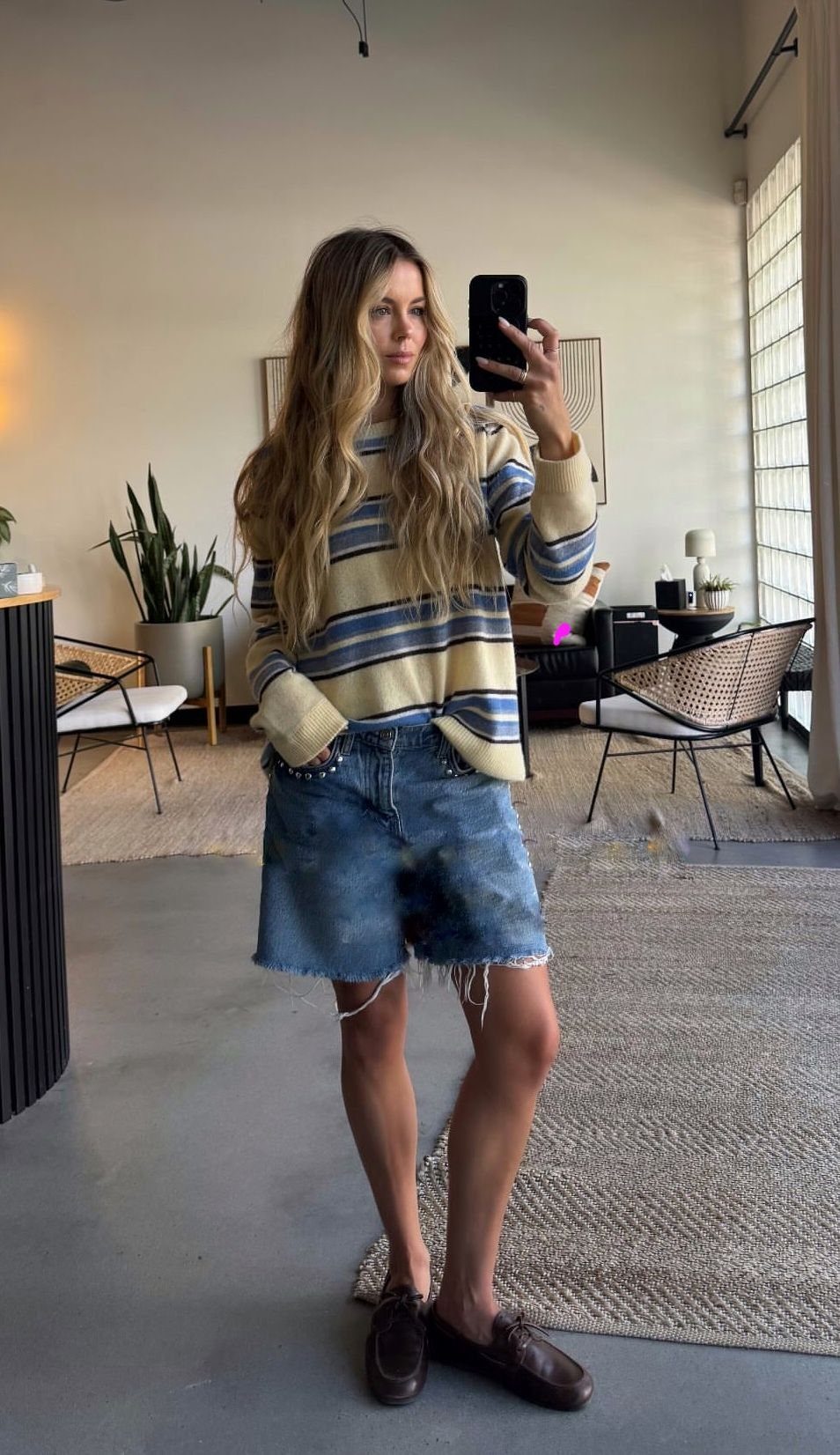 Woman posing in a striped rugby sweater, long denim shorts, and brown boat shoes.