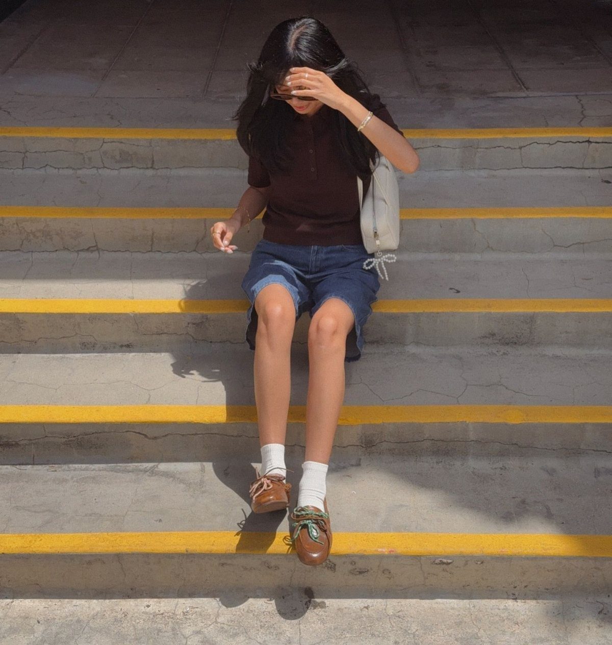 Person sitting on stairs wearing a brown polo shirt, denim shorts, and brown boat shoes.