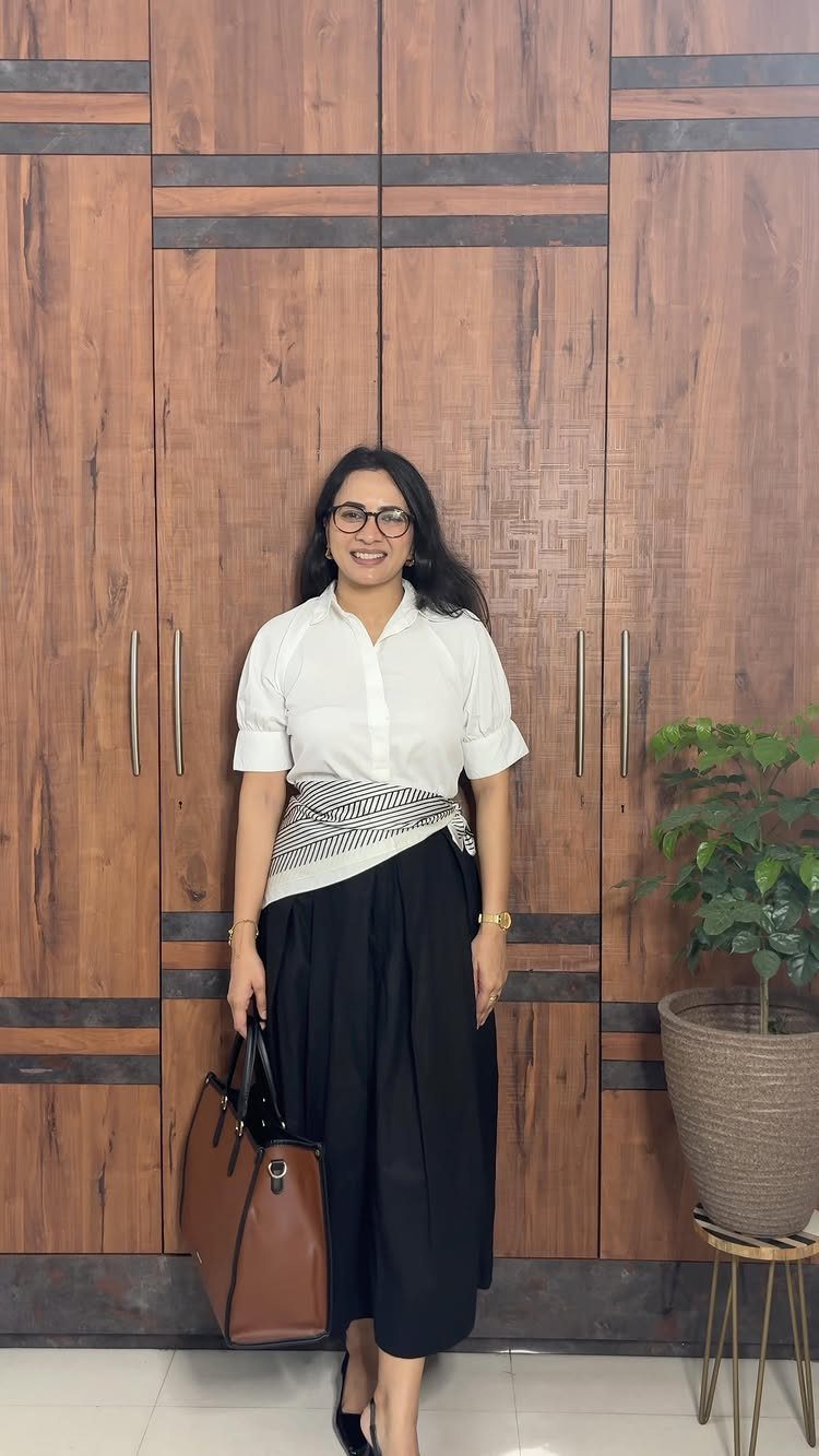 Woman wearing a crisp white shirt and long black skirt holding a brown leather bag.