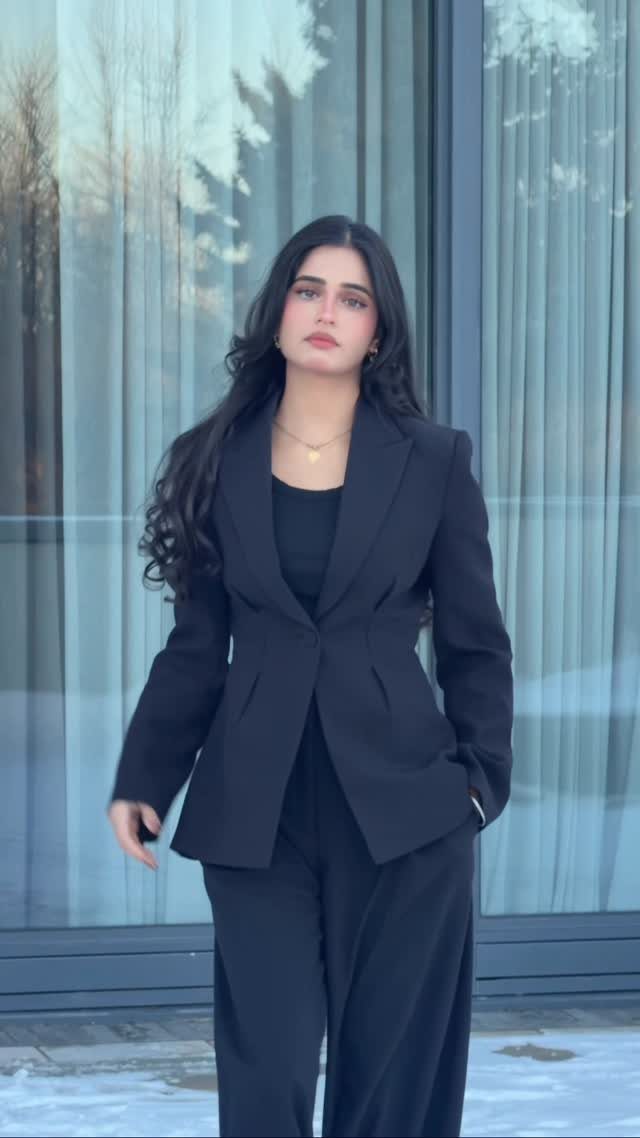 Woman posing in a black structured blazer and matching wide-leg trousers outdoors.
