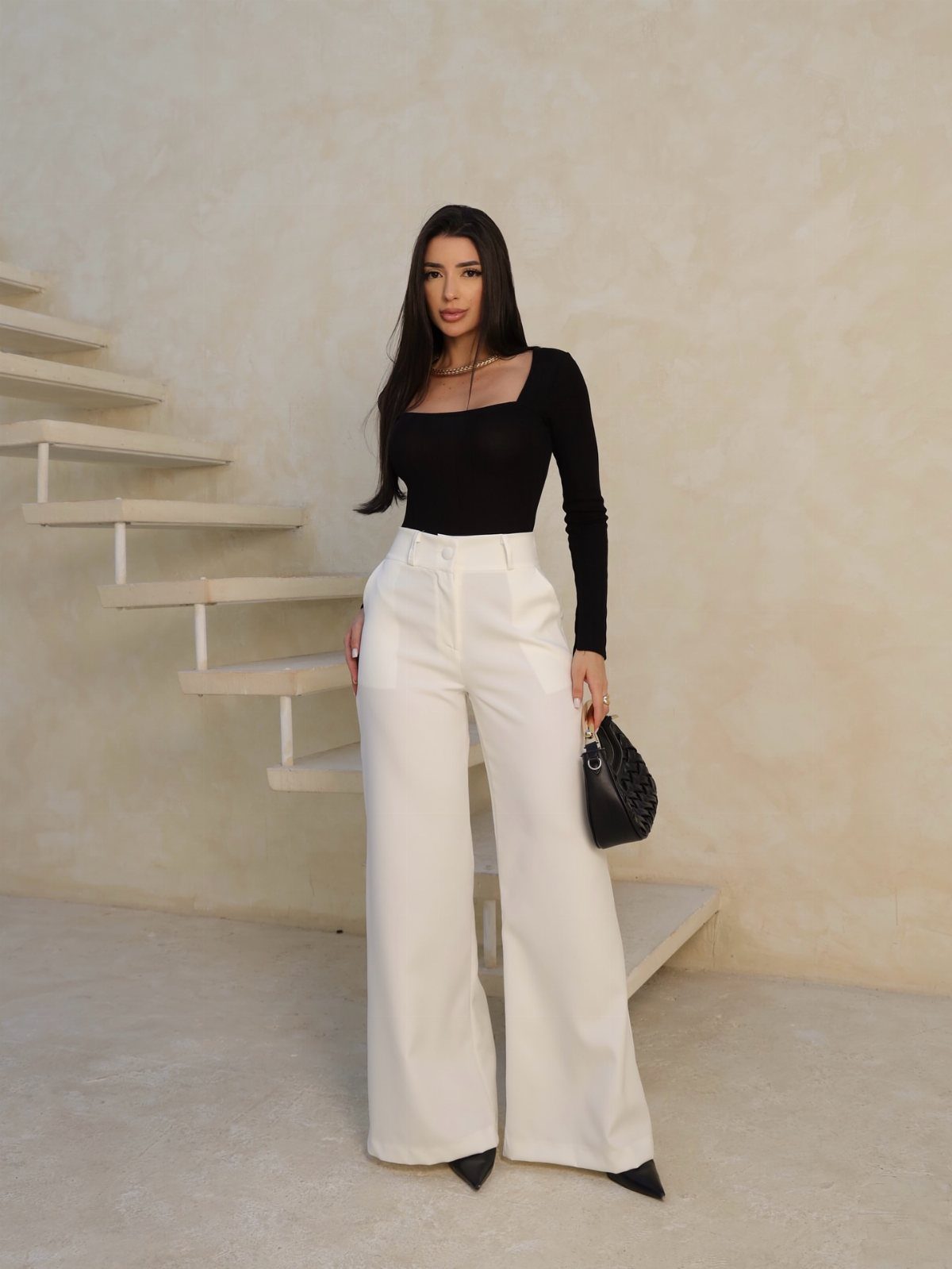 Woman posing in a black long-sleeved top and white wide-leg trousers.