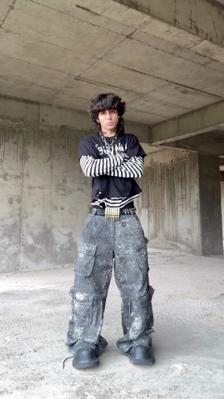 A person posing in patterned cargo pants and a black and white striped shirt with a large buckle belt.