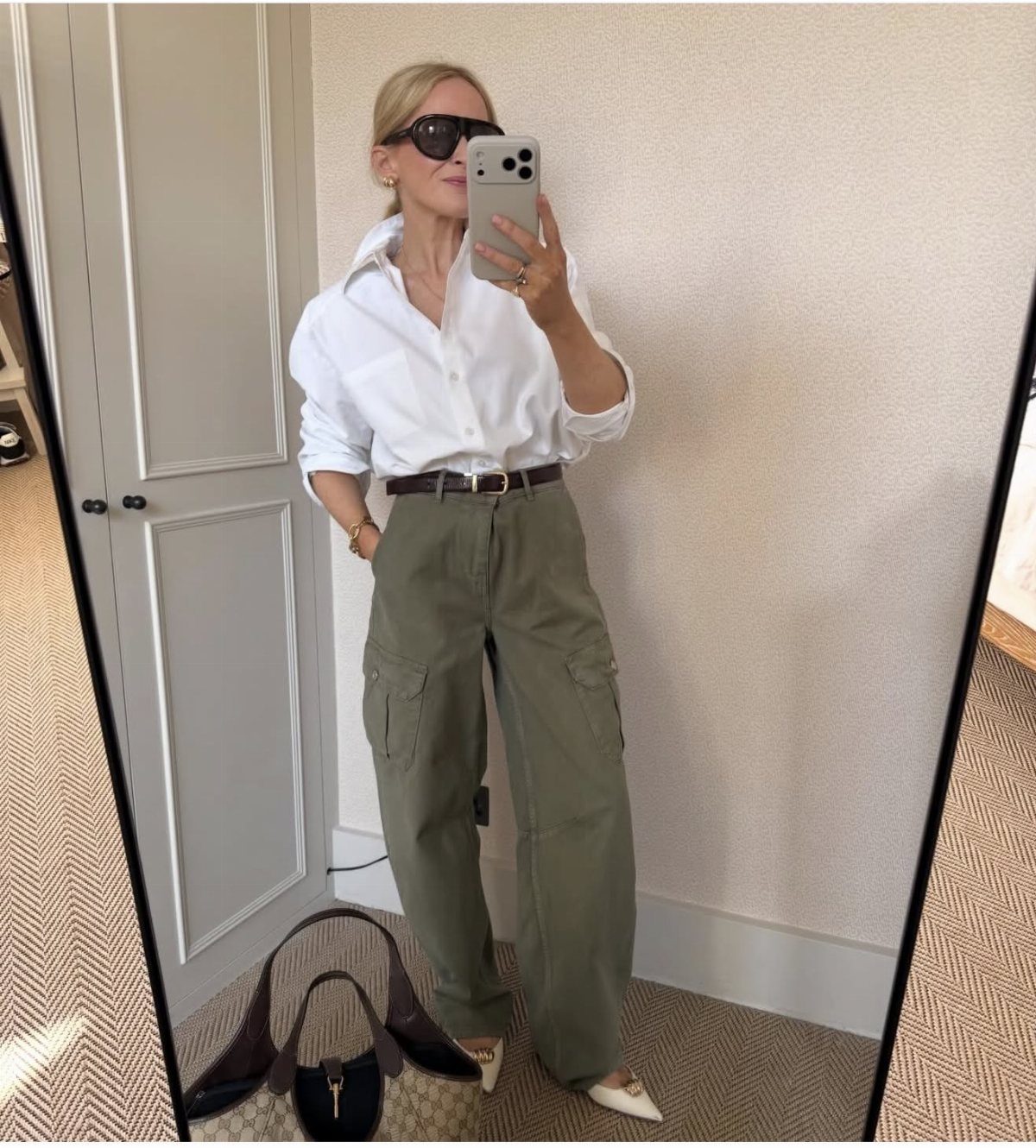 Woman in olive cargo pants and a white button-up shirt posing for a mirror selfie.
