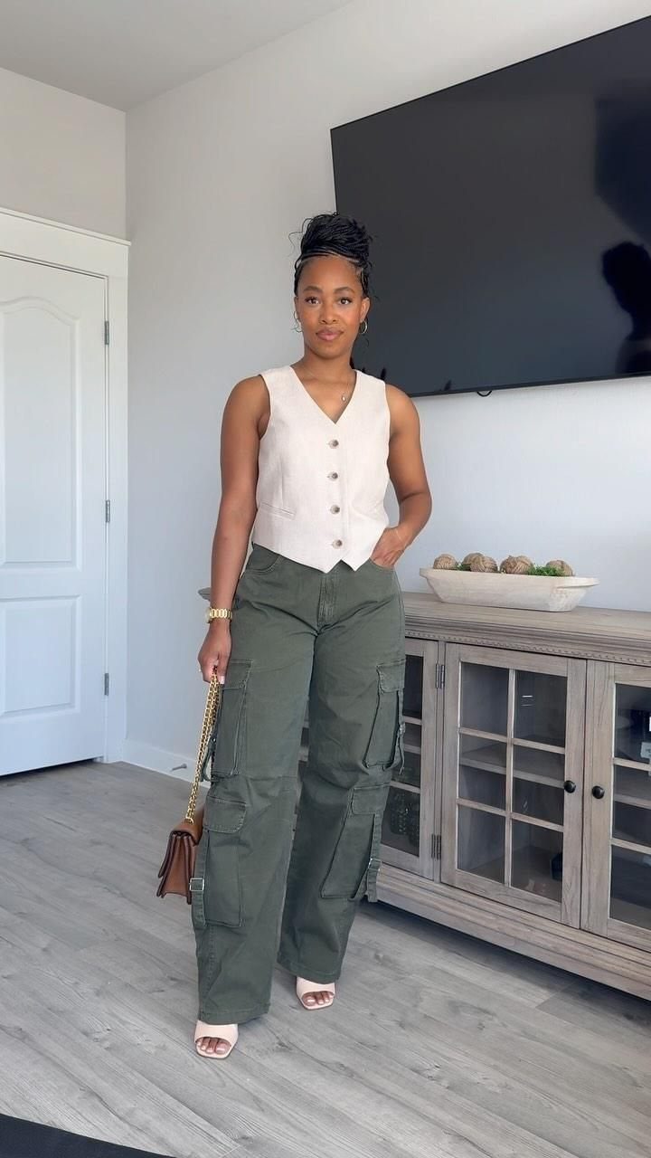 A woman posing in olive green cargo pants and a cream sleeveless vest.
