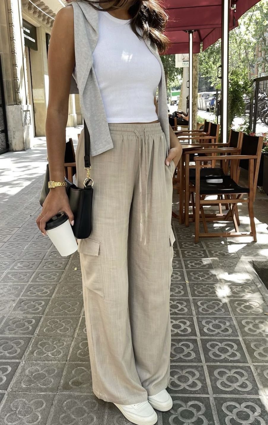 Person wearing beige linen cargo pants, a white tank top, and a grey vest on a sidewalk.