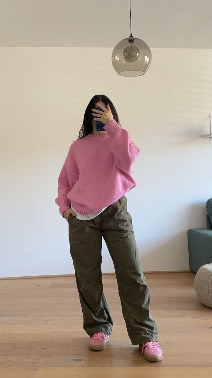 Person wearing a pink chunky sweater, olive cargo pants, and pink sneakers standing indoors.