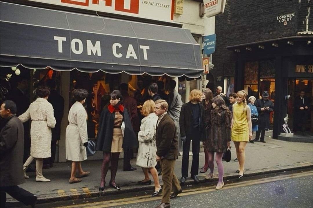 People in 1960s fashion standing outside the Tom Cat boutique on a city street.