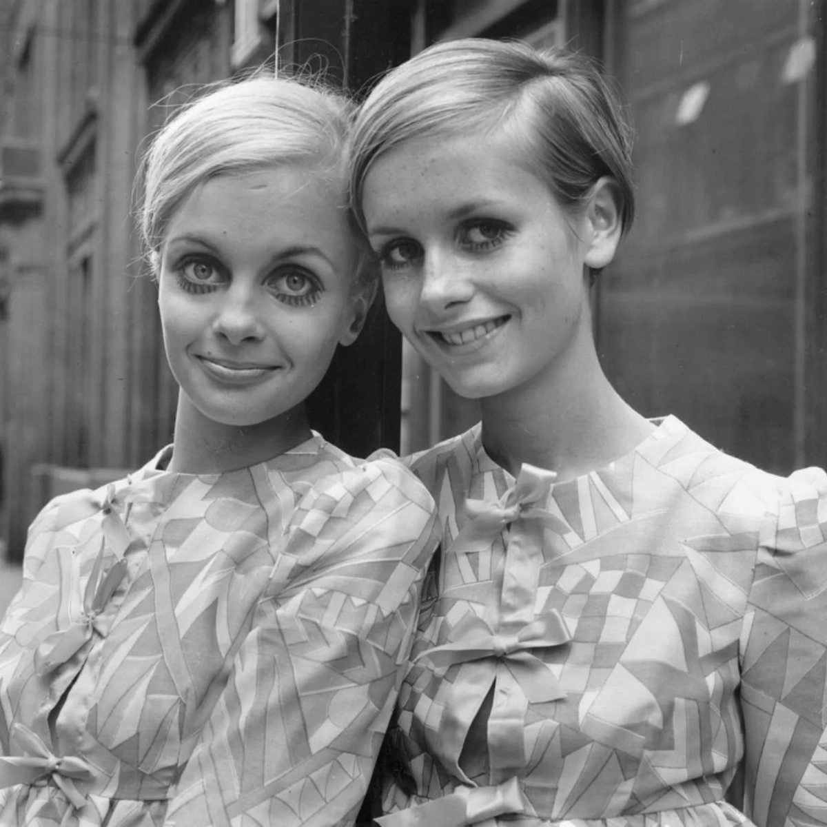 Two young women with 1960s mod makeup and patterned dresses posing together.