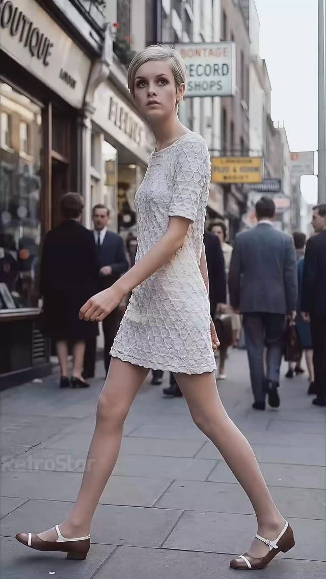 A young woman in a white lace mini dress walking through a busy London street.
