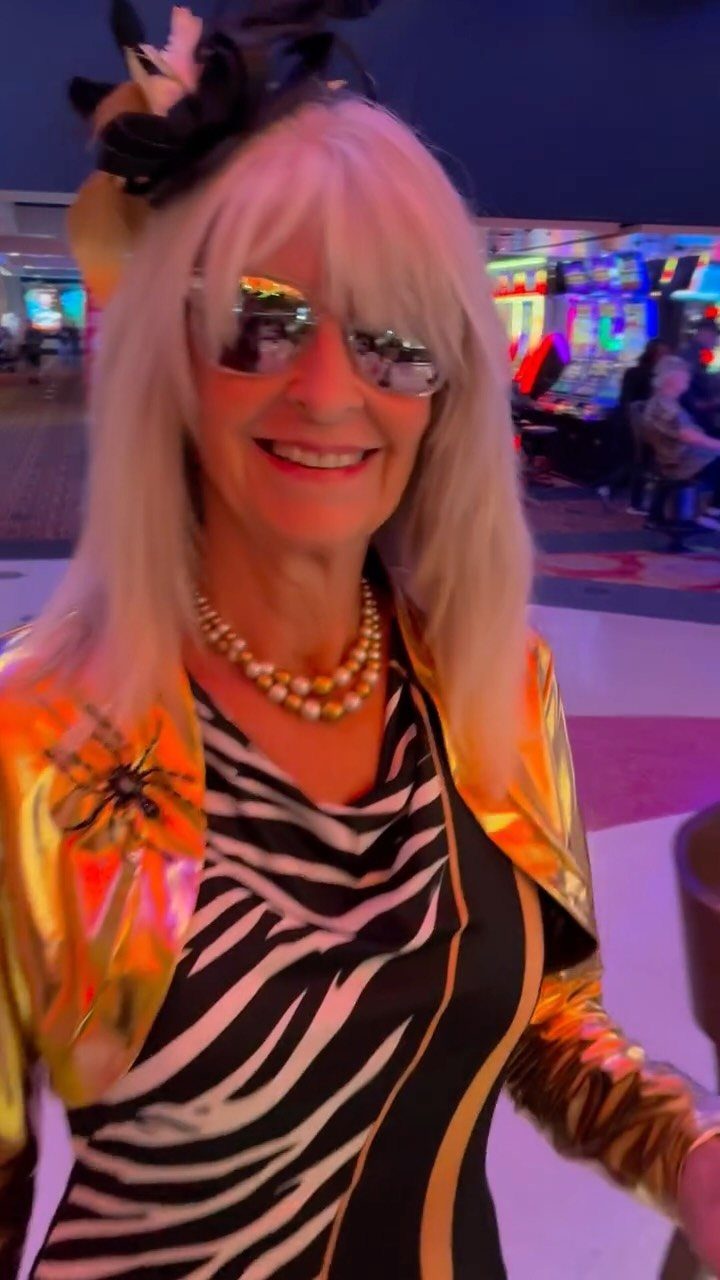 Smiling woman with silver hair wearing a zebra print top and a gold jacket in a casino.