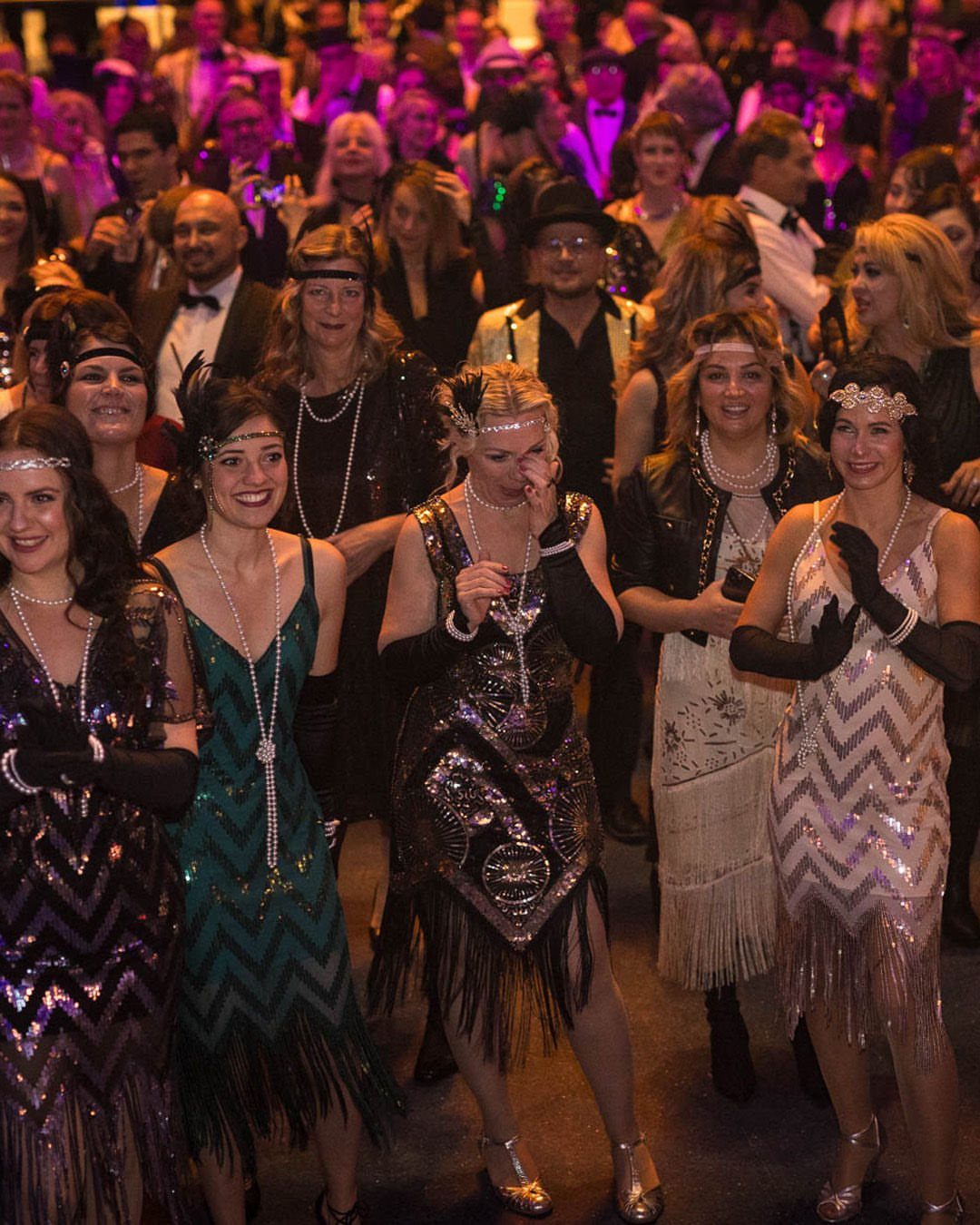Women wearing vintage-inspired flapper dresses with sequins and fringe at a social event.