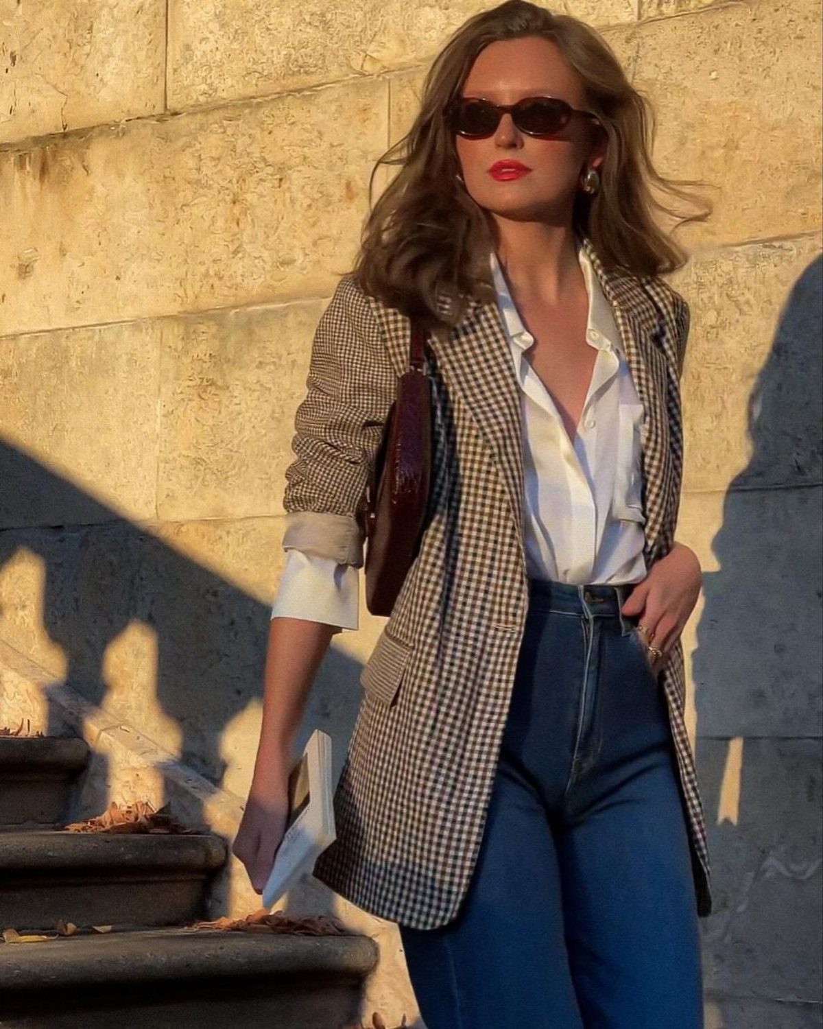 Woman in a checkered plaid blazer, white shirt, and high-waisted blue denim jeans standing outdoors.