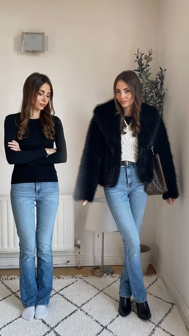 Two women posing indoors, one wearing a voluminous black faux fur coat and blue jeans.