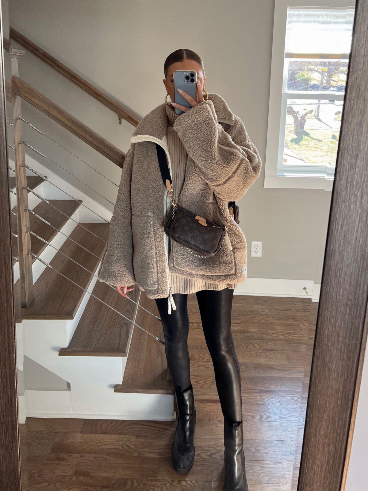 A person posing in a teddy coat, oversized sweater, and faux leather leggings.