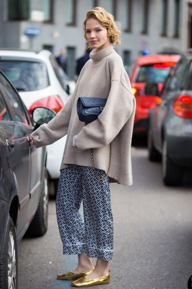 Woman wearing an oversized beige turtleneck sweater and patterned blue silk trousers on a city street.