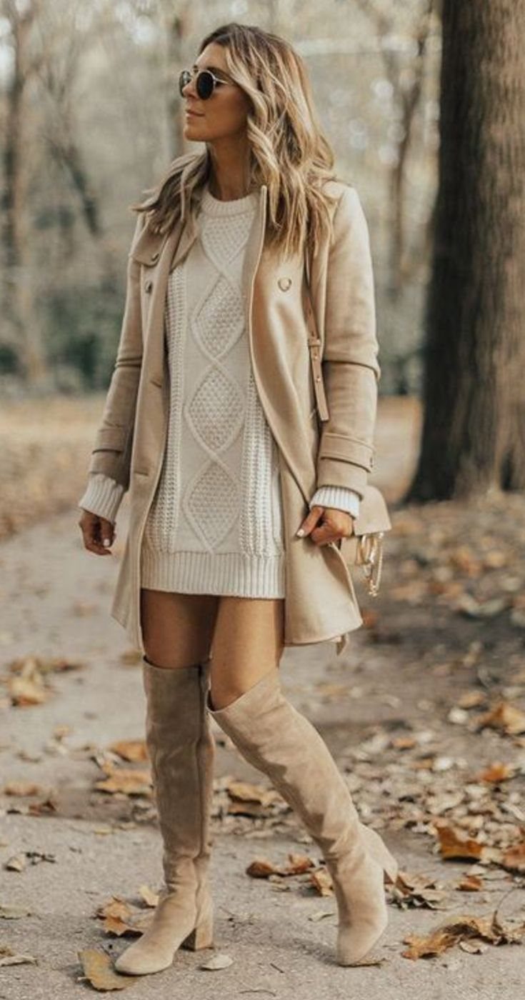 Woman wearing a cream sweater dress, tan coat, and beige over-the-knee boots in a forest.